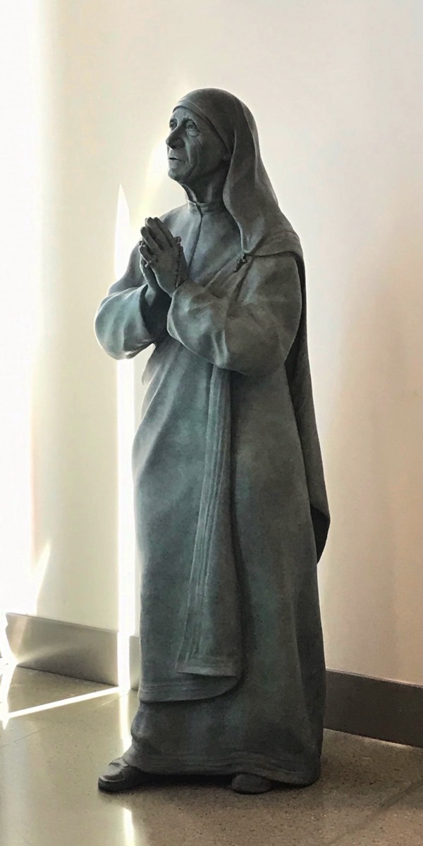 Mother Teresa life-size bronze statue looking up holding rosary beads in moment of thought