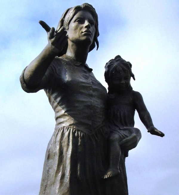 Over life size bronze statue of mother and child pioneer. Mother is sowing seeds with baby in arms.