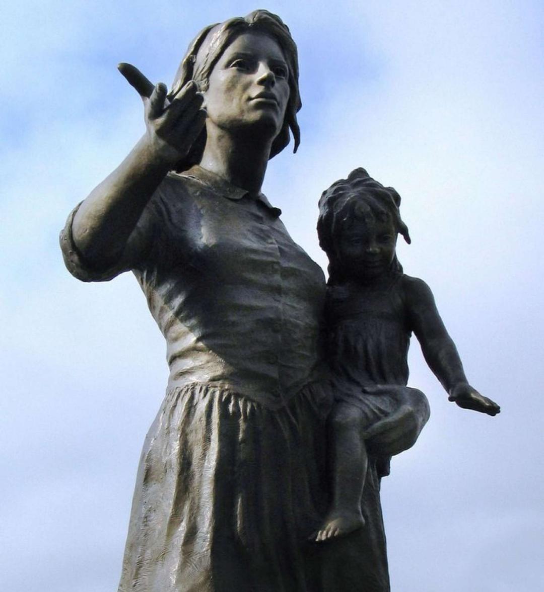Bronze pioneer woman sowing seeds while holding child in her arms